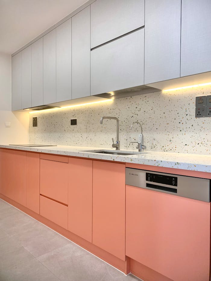 A sleek modern kitchen interior featuring minimalist pink cabinets and speckled backsplash with integrated lighting.